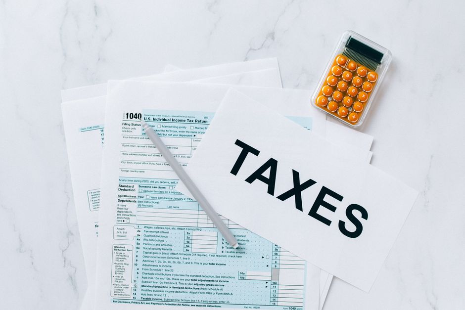 A close-up image of various printed tax and financial documents consisting of multiple pages laid flat on a green surface, with some pages overlapping each other. On top of the documents, there are sm